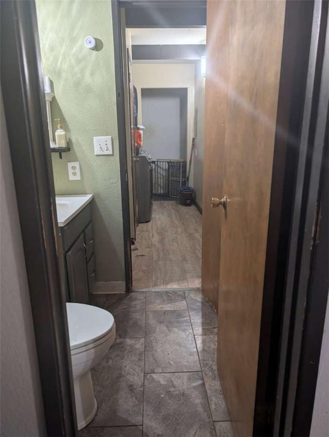 half bath with toilet, a textured wall, vanity, and baseboards
