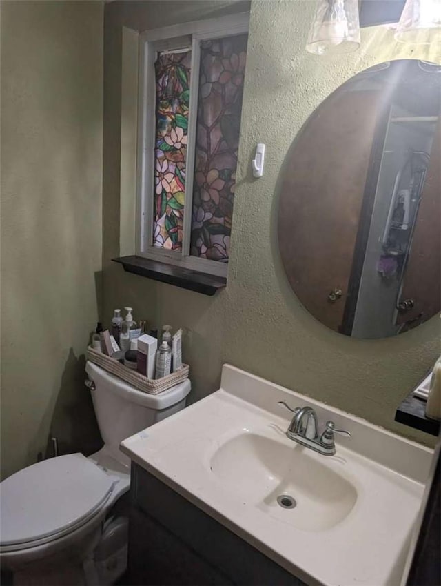 bathroom featuring toilet, a textured wall, and vanity
