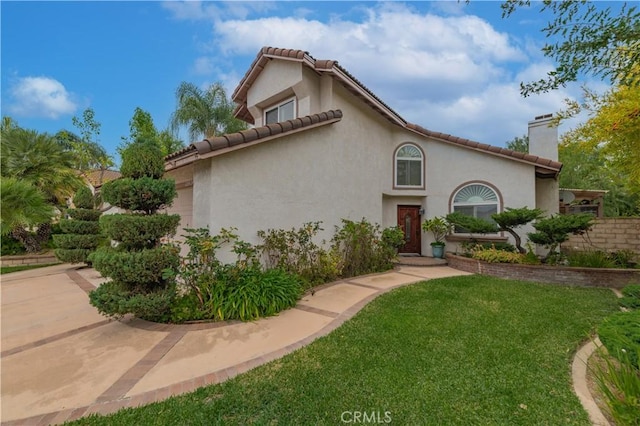 mediterranean / spanish-style house with a tiled roof, a chimney, a front lawn, and stucco siding