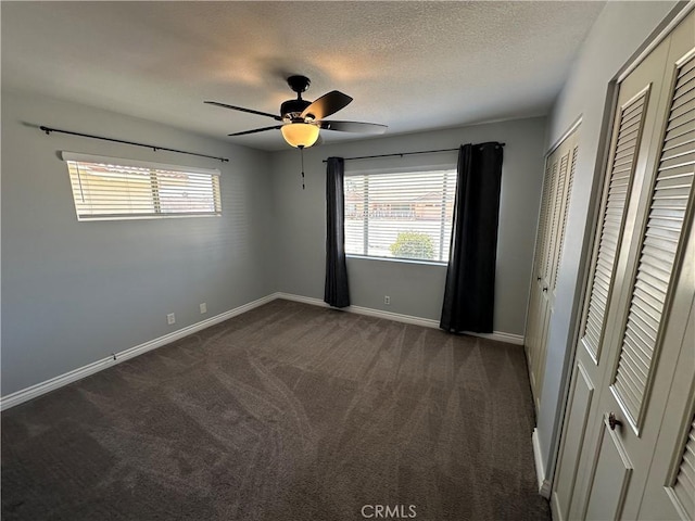 unfurnished bedroom with two closets, baseboards, multiple windows, and dark colored carpet