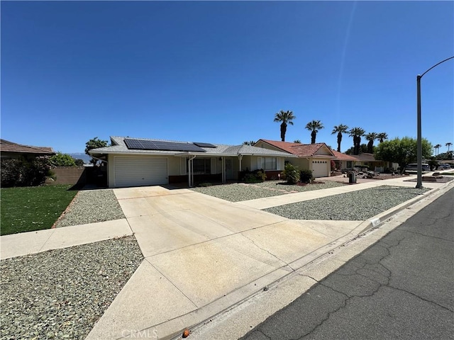 ranch-style house featuring an attached garage, roof mounted solar panels, and concrete driveway