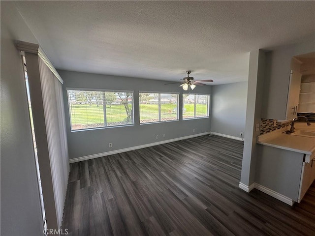 unfurnished living room with dark wood-style flooring, ceiling fan, baseboards, and a sink