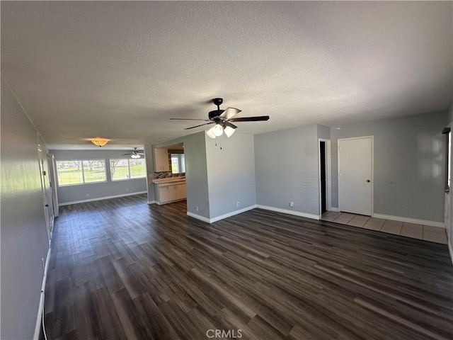 unfurnished living room with a textured ceiling, ceiling fan, baseboards, and dark wood-style flooring