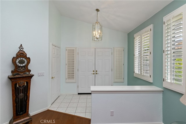 foyer featuring light wood-style flooring, baseboards, a chandelier, and vaulted ceiling