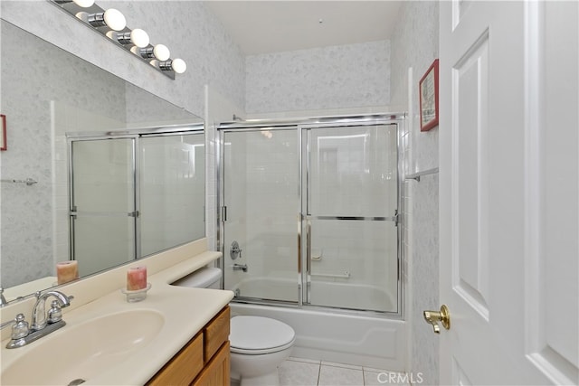 bathroom with bath / shower combo with glass door, toilet, vanity, wallpapered walls, and tile patterned flooring