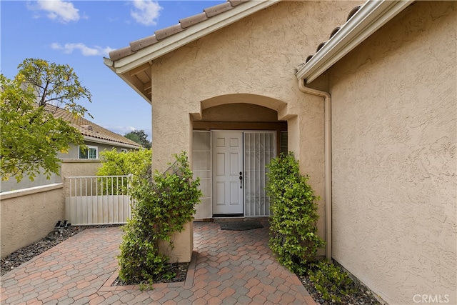 view of exterior entry with a patio, stucco siding, and fence