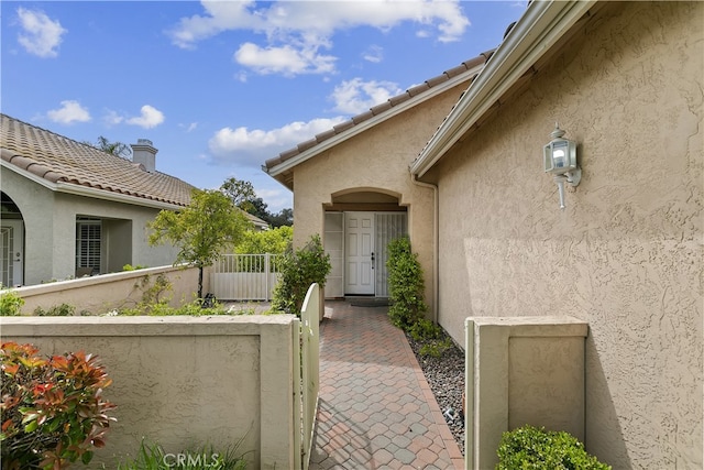 doorway to property with stucco siding, fence, and a gate