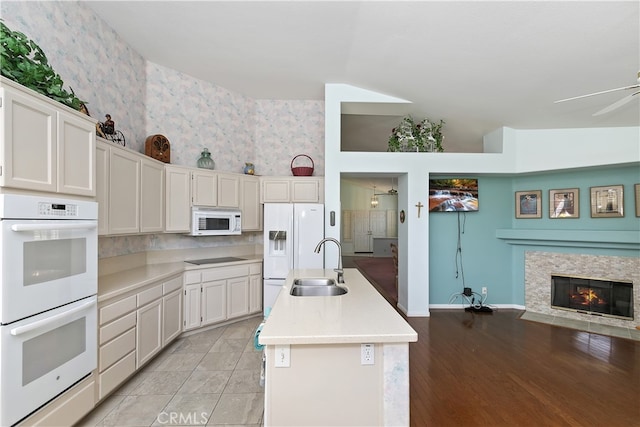 kitchen featuring an island with sink, white appliances, light countertops, a sink, and wallpapered walls