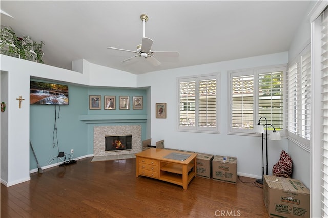 living room with baseboards, vaulted ceiling, a tiled fireplace, a ceiling fan, and wood finished floors