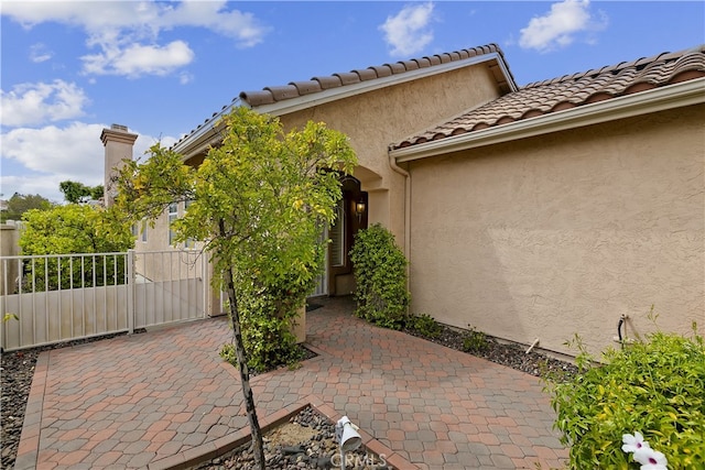 view of exterior entry featuring a patio, stucco siding, fence, and a tile roof