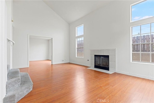 unfurnished living room featuring high vaulted ceiling, a fireplace, light wood-style floors, and baseboards