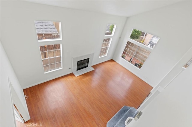 unfurnished living room featuring a high ceiling, wood finished floors, a tiled fireplace, and baseboards