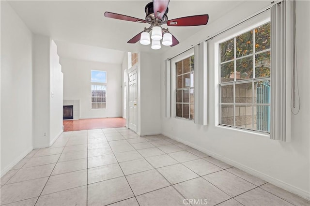 tiled spare room featuring baseboards, a ceiling fan, and a fireplace