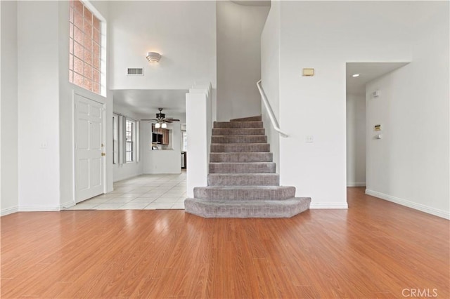 entryway with stairway, a towering ceiling, a ceiling fan, and light wood-style flooring