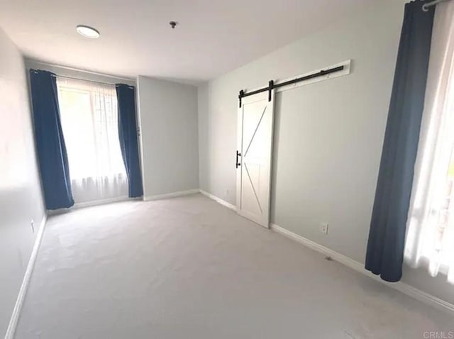 unfurnished bedroom with light colored carpet, a barn door, and baseboards