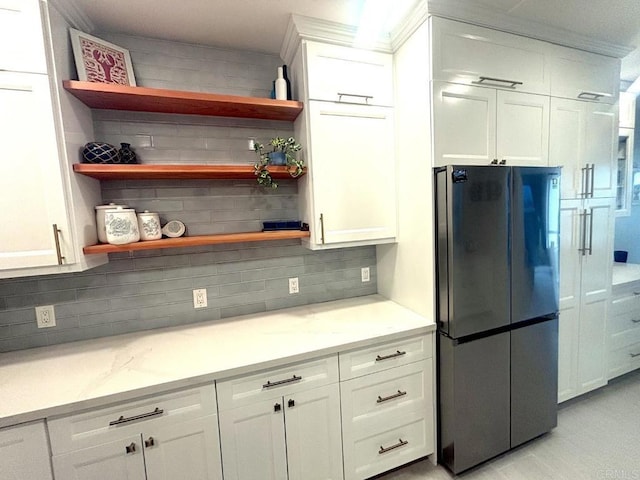 kitchen with freestanding refrigerator, light stone countertops, white cabinetry, open shelves, and backsplash