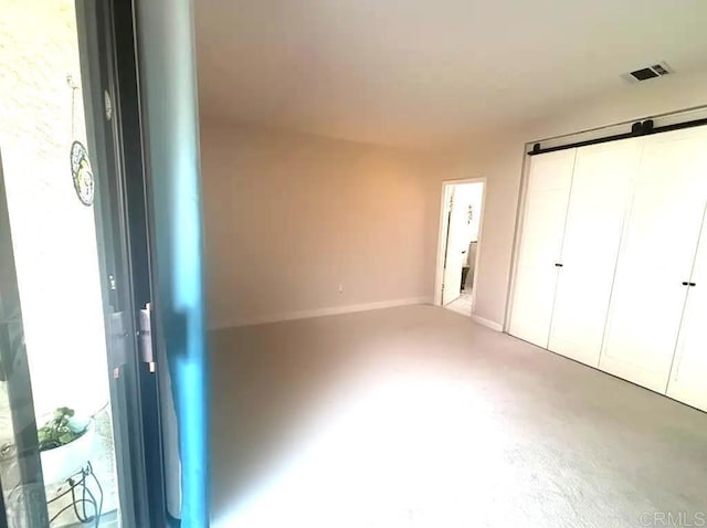 unfurnished bedroom with baseboards, a barn door, a closet, and visible vents