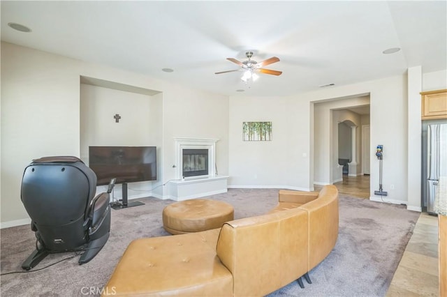 living room with a glass covered fireplace, baseboards, light carpet, visible vents, and ceiling fan