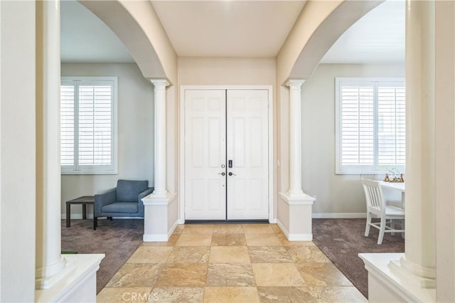 entrance foyer featuring light carpet, arched walkways, and ornate columns