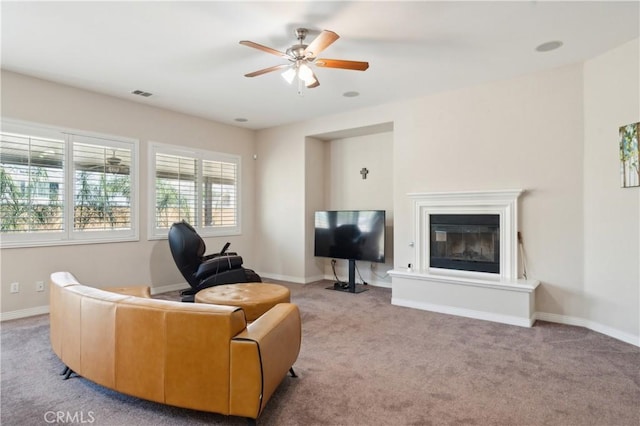 carpeted living room featuring visible vents, ceiling fan, a glass covered fireplace, and baseboards