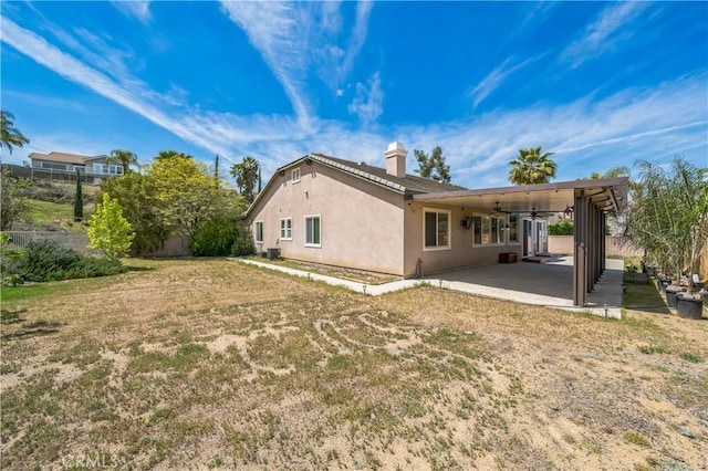 back of property featuring stucco siding, a ceiling fan, a lawn, a patio, and a chimney