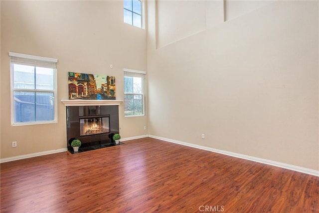 unfurnished living room with a fireplace, a towering ceiling, baseboards, and wood finished floors