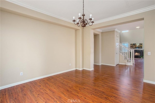 spare room with baseboards, a warm lit fireplace, ornamental molding, a chandelier, and wood finished floors