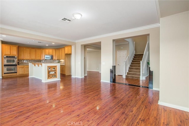 unfurnished living room featuring visible vents, baseboards, ornamental molding, wood finished floors, and stairs