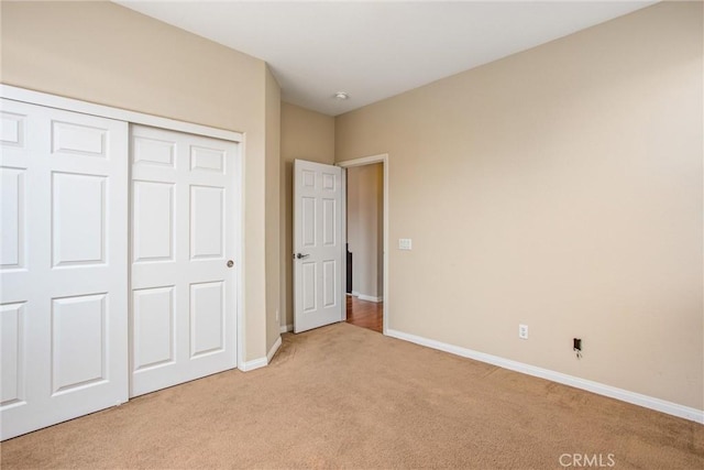 unfurnished bedroom featuring a closet, baseboards, and light colored carpet