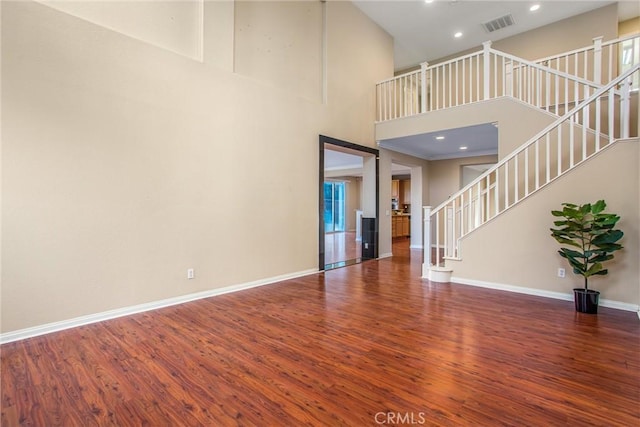 unfurnished living room with a towering ceiling, baseboards, stairs, visible vents, and wood finished floors