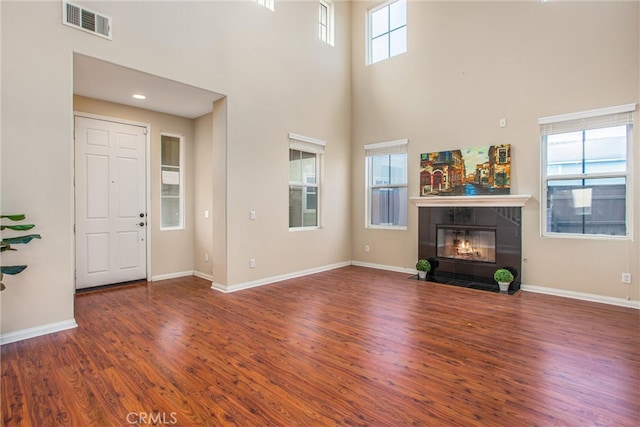 unfurnished living room with a tiled fireplace, visible vents, a high ceiling, and wood finished floors