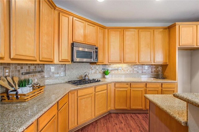 kitchen featuring dark wood-type flooring, appliances with stainless steel finishes, backsplash, and light stone countertops