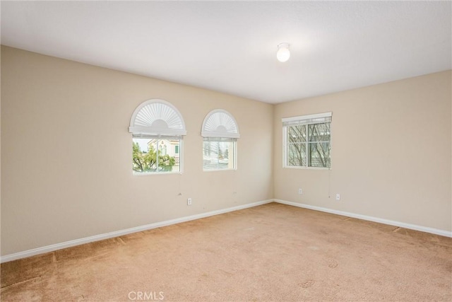 spare room featuring light carpet and baseboards