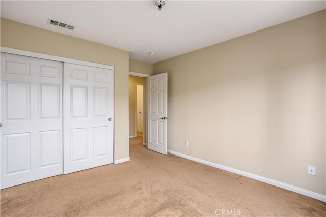 unfurnished bedroom featuring visible vents, baseboards, a closet, and light carpet