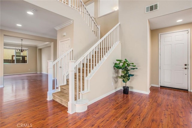 entryway with a chandelier, stairway, crown molding, visible vents, and wood finished floors