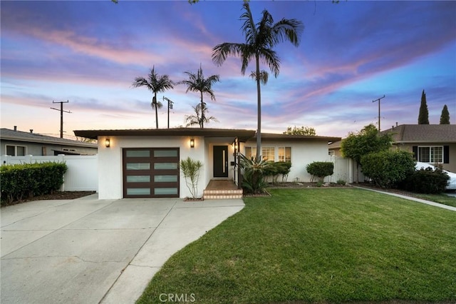 view of front of home featuring an attached garage, fence, stucco siding, a front lawn, and driveway