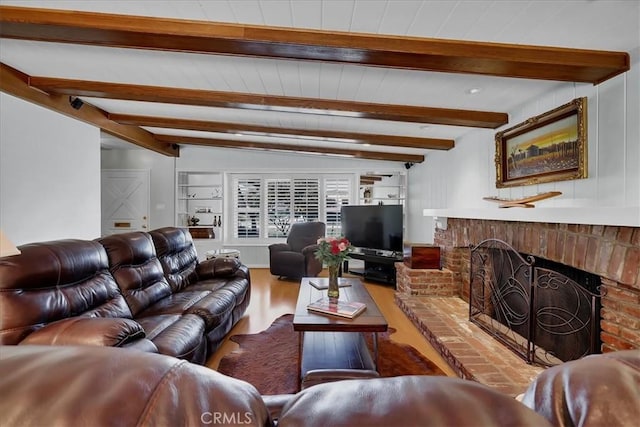 living area featuring beamed ceiling, wood finished floors, and a brick fireplace