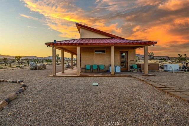 53105 Chia Trl, Pioneertown, CA 92268 - back of house at dusk with a jacuzzi, a patio, metal roof, and stucco siding