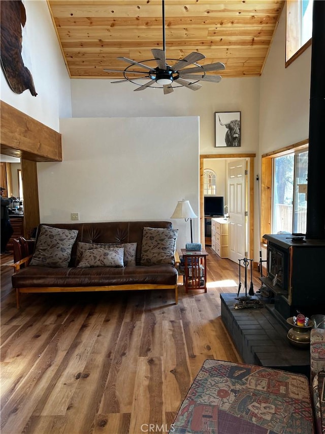 living room featuring high vaulted ceiling, ceiling fan, a wood stove, wooden ceiling, and wood finished floors