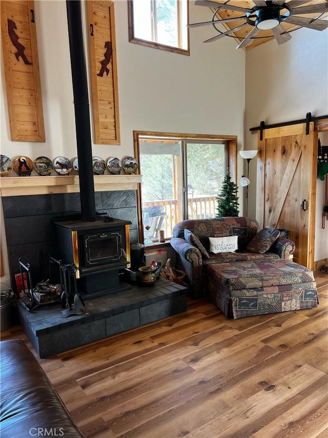 living room featuring a wood stove, a towering ceiling, ceiling fan, and wood finished floors