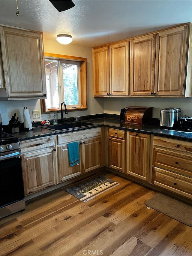 kitchen featuring dark wood-style floors, a sink, range with gas stovetop, and dark countertops