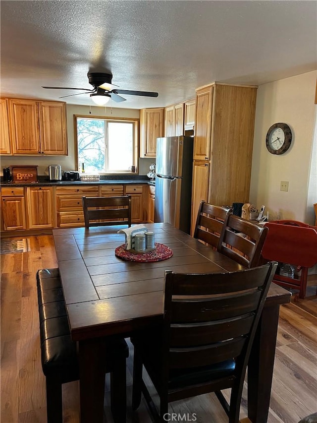 dining space featuring light wood-style flooring, a ceiling fan, and a textured ceiling