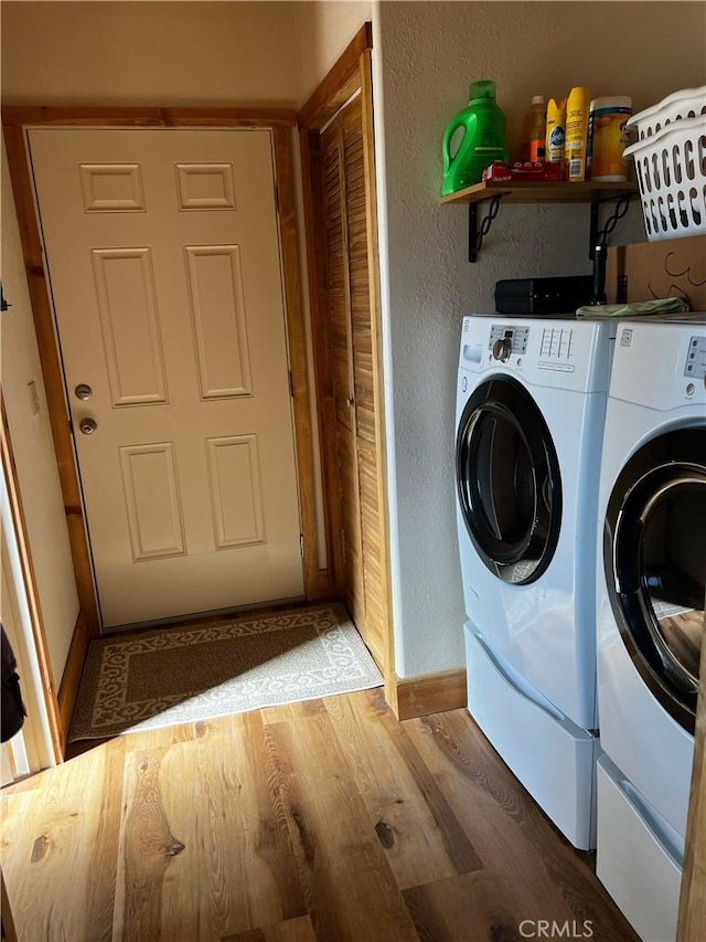 washroom featuring baseboards, a textured wall, laundry area, light wood finished floors, and washer and clothes dryer