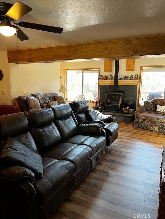 living room with a wood stove, wood finished floors, a ceiling fan, and a healthy amount of sunlight