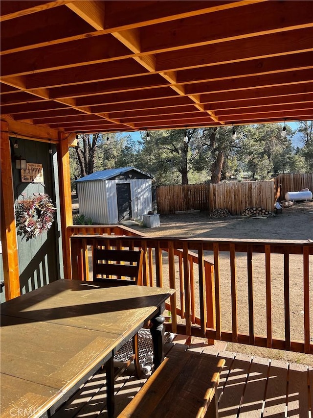 wooden deck featuring outdoor dining space, fence, an outbuilding, and a storage unit