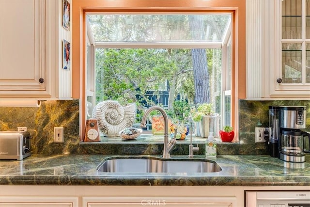 kitchen with tasteful backsplash, glass insert cabinets, cream cabinetry, a healthy amount of sunlight, and a sink