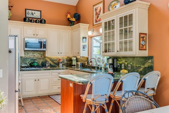 kitchen featuring glass insert cabinets, a sink, a peninsula, stainless steel appliances, and backsplash