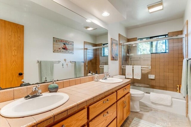 bathroom with double vanity, a sink, toilet, and enclosed tub / shower combo