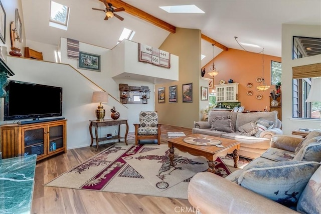 living room featuring high vaulted ceiling, ceiling fan, a skylight, wood finished floors, and beam ceiling