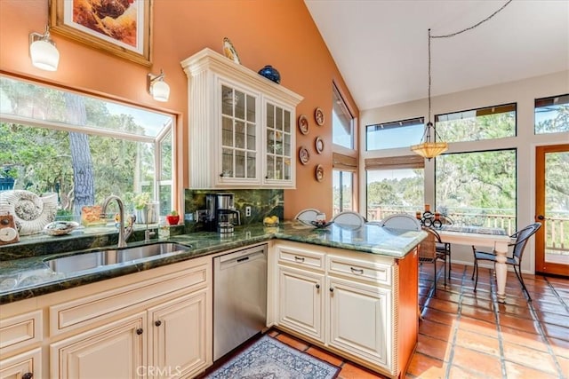 kitchen featuring dark stone countertops, glass insert cabinets, dishwasher, a sink, and pendant lighting